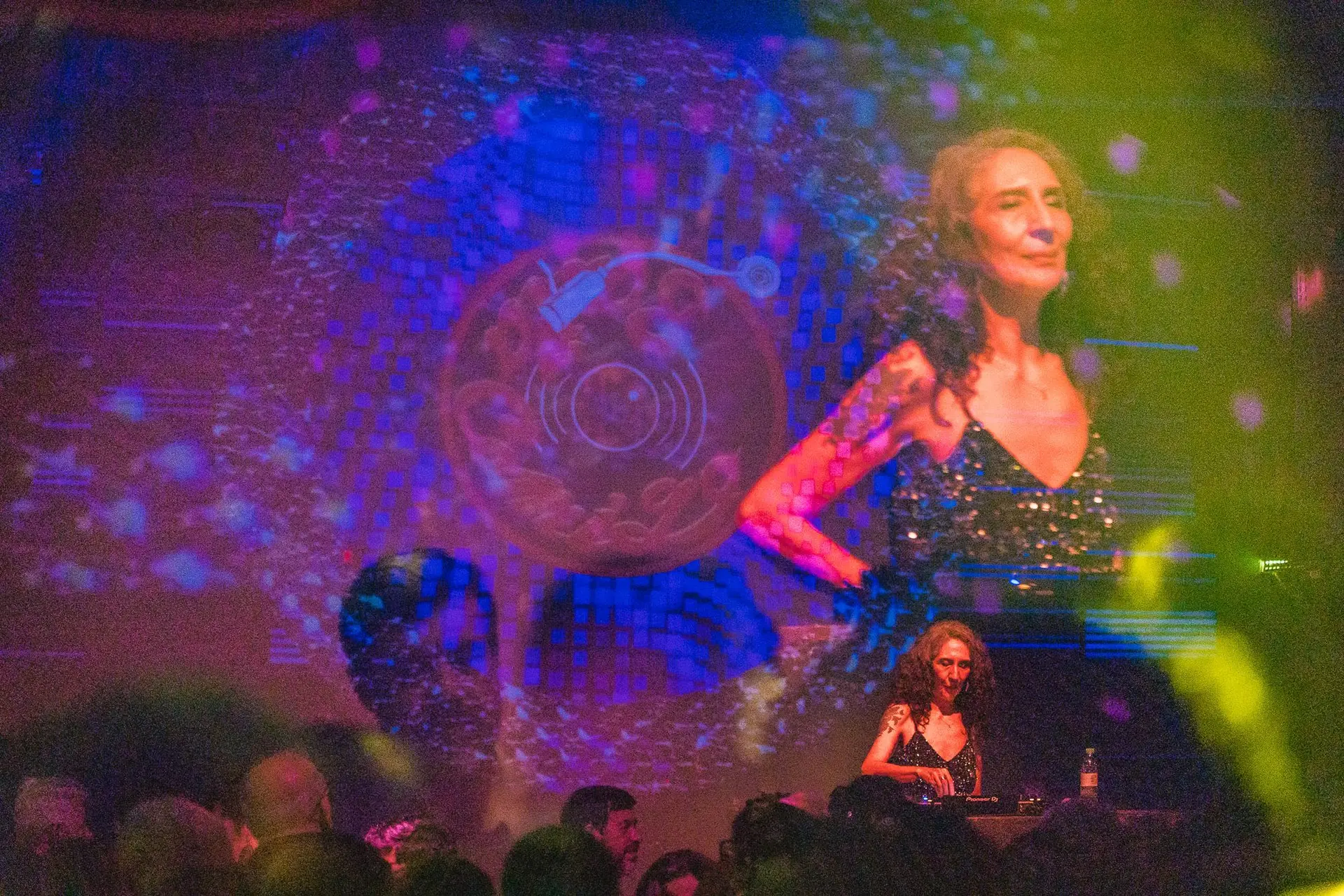 Kátia Suman na cabine de DJ, com o público à frente e a projeção da Baila Comigo ao fundo
